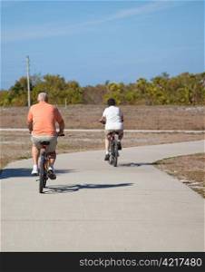 Rear view of a senior couple riding their bicycles. Focus on the husband, in the foreground.