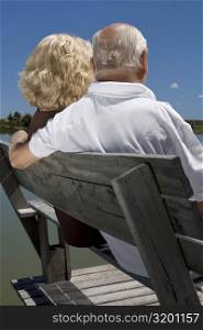 Rear view of a senior couple sitting on a bench at the lakeside