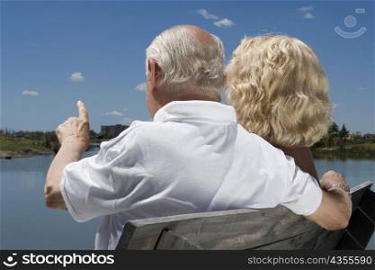 Rear view of a senior couple sitting on a bench at the lakeside