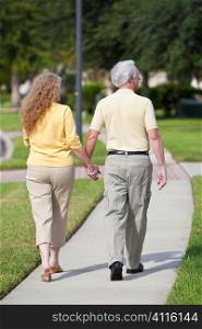 Rear view of a senior retired man and woman couple walking and holding hands happy together.