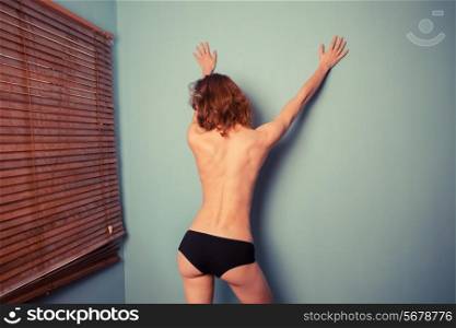Rear view of a slender topless woman striking a sexy pose against a blue wall