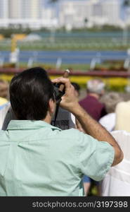 Rear view of a spectator looking through a pair of binoculars at the horseracing track