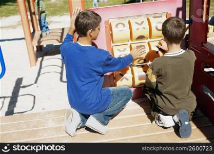 Rear view of a teenage boy and a boy playing tic-tac-toe