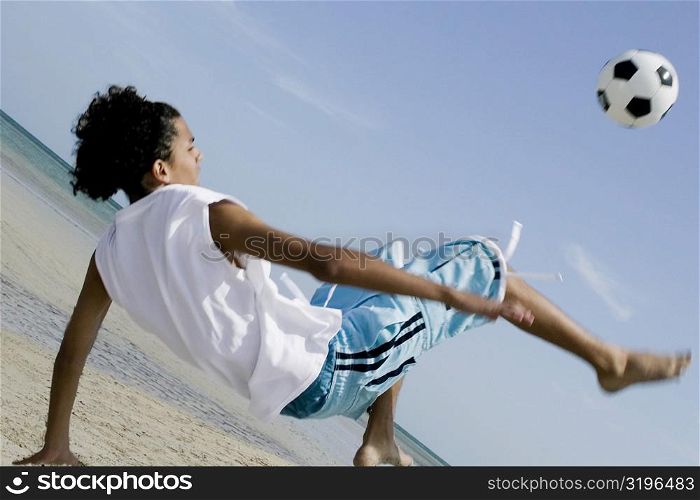 Rear view of a teenage boy playing with a soccer ball on the beach