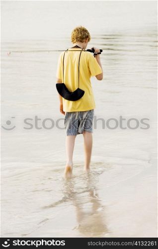 Rear view of a teenage boy walking in a lake with a fishing rod