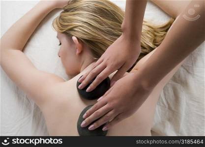 Rear view of a teenage girl getting a back massage with therapeutic stones