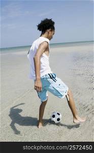 Rear view of a teenage girl playing with a soccer ball on the beach
