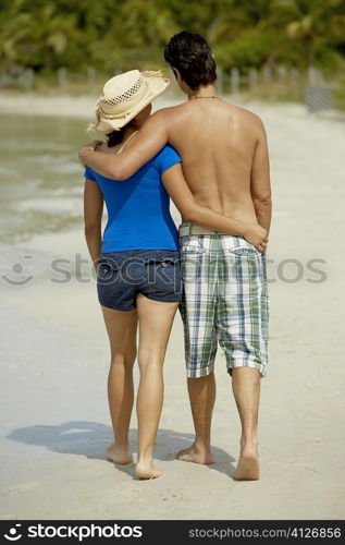 Rear view of a teenage girl walking on the beach with her arm around a young man