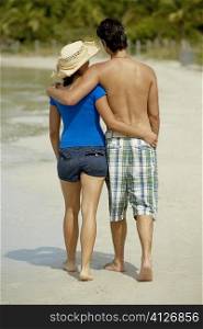 Rear view of a teenage girl walking on the beach with her arm around a young man