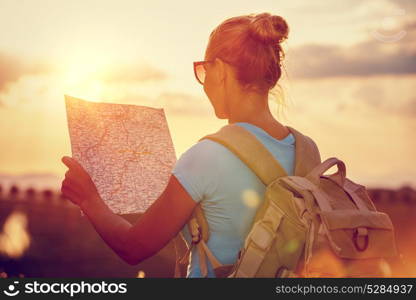 Rear view of a traveler girl with backpack exploring map, enjoying mild sunset light, active people lifestyle, summer fun vacation, traveling around the world