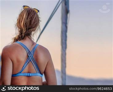 Rear view of a woman on sailboat enjoying beautiful view of mild sunset light. Peaceful yacht travel.. Pretty woman enjoying beautiful sunset view