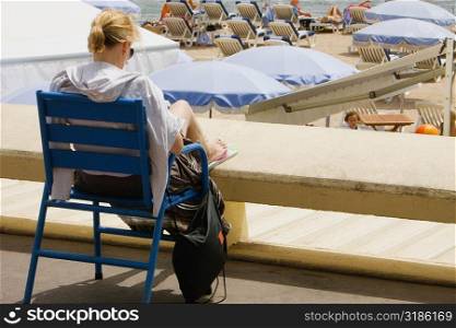 Rear view of a woman sitting in an armchair on the beach, Plage De La Croisette, Cote d&acute;Azur, Cannes, Provence-Alpes-Cote D&acute;Azur, France