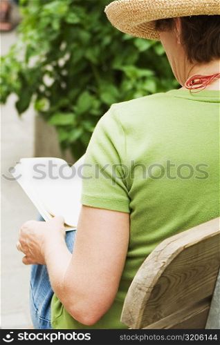Rear view of a woman sitting on a bench and reading a book, Cinque Terre, Manarola, La Spezia, Liguria, Italy