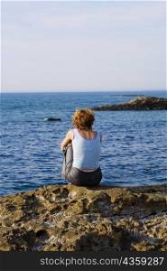 Rear view of a woman sitting on a rock, Baie de Biarritz, Biarritz, Pyrenees-Atlantiques, France