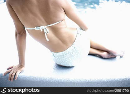 Rear view of a woman sitting on the ledge of a swimming pool