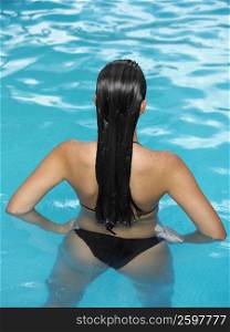 Rear view of a woman standing in water with arms akimbo