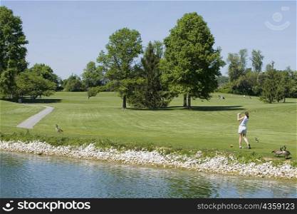 Rear view of a woman swinging a golf club near a lake