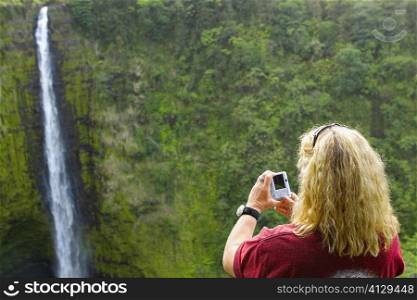Rear view of a woman taking a photograph of a waterfall, Akaka Falls, Akaka Falls State Park, Hilo, Big Island, Hawaii Islands, USA