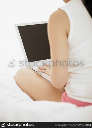Rear view of a woman using a laptop on the bed