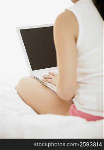 Rear view of a woman using a laptop on the bed