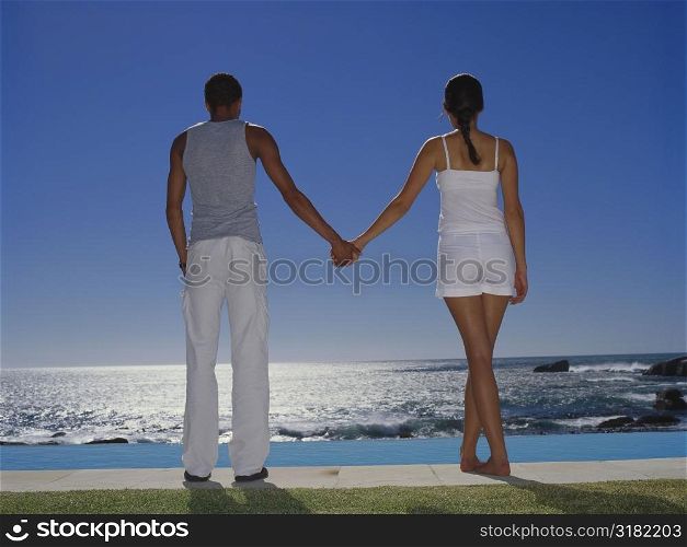 Rear view of a young couple holding hands and standing by the pool