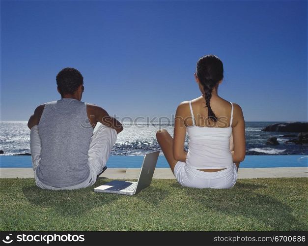 Rear view of a young couple sitting beside a swimming pool