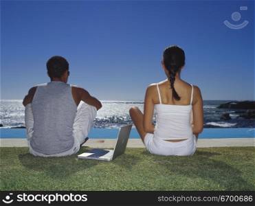 Rear view of a young couple sitting beside a swimming pool