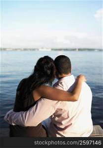 Rear view of a young couple sitting on a pier with their arms around each other