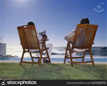 Rear view of a young couple sitting together reading newspapers