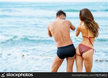 Rear view of a young couple with beautiful bodies in swimwear having fun on a tropical beach. Young couple with beautiful bodies in swimwear having fun on a tropical beach