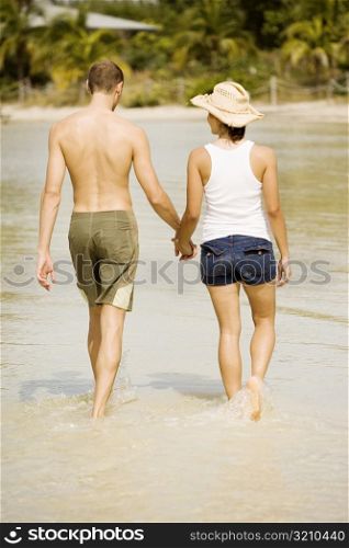 Rear view of a young man and a teenage girl holding hands walking on the beach
