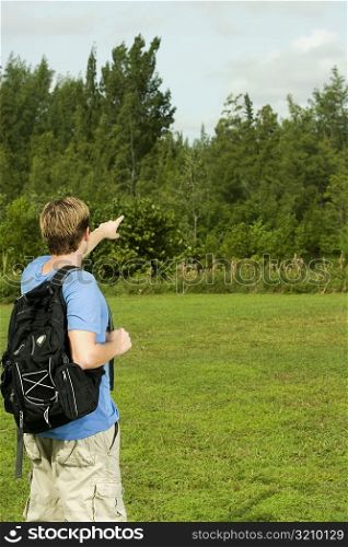 Rear view of a young man carrying a backpack and pointing forward