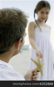 Rear view of a young man giving a starfish to a girl
