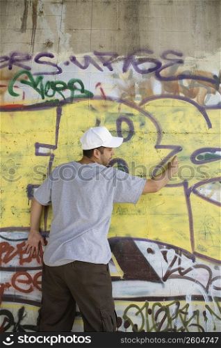 Rear view of a young man making a graffiti on a wall