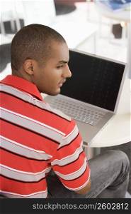Rear view of a young man sitting at a cafe with a laptop in front of him