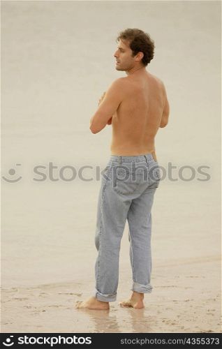 Rear view of a young man standing on the beach and looking sideways