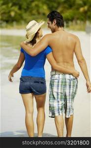 Rear view of a young man walking on the beach with his arm around a teenage girl