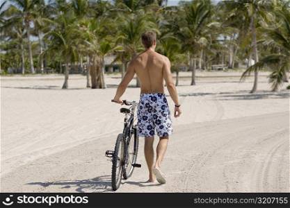 Rear view of a young man walking with a bicycle on the beach