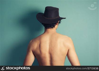Rear view of a young shirtless man wearing acowboy hat