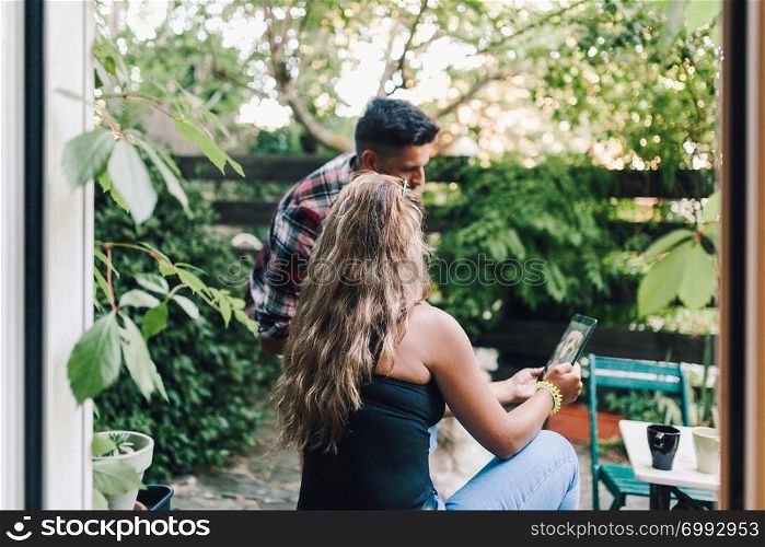 Rear view of a young smiling couple sitting on the steps outside the wooden hut taking a picture of their dog