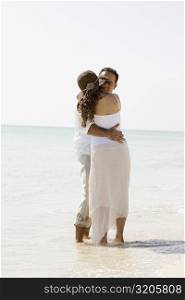 Rear view of a young woman and a mid adult man embracing each other on the beach