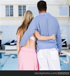 Rear view of a young woman and a mid adult man standing at the poolside
