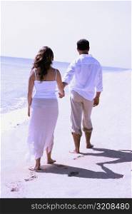 Rear view of a young woman and a mid adult man walking on the beach
