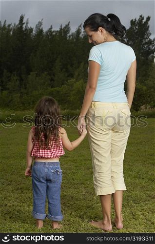 Rear view of a young woman holding her daughter&acute;s hand and standing on the lawn