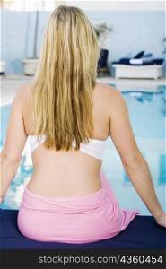 Rear view of a young woman sitting at the poolside