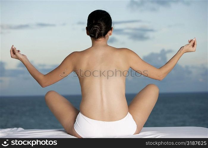 Rear view of a young woman sitting in a lotus position with her arms outstretched