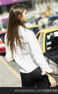 Rear view of a young woman standing at the roadside
