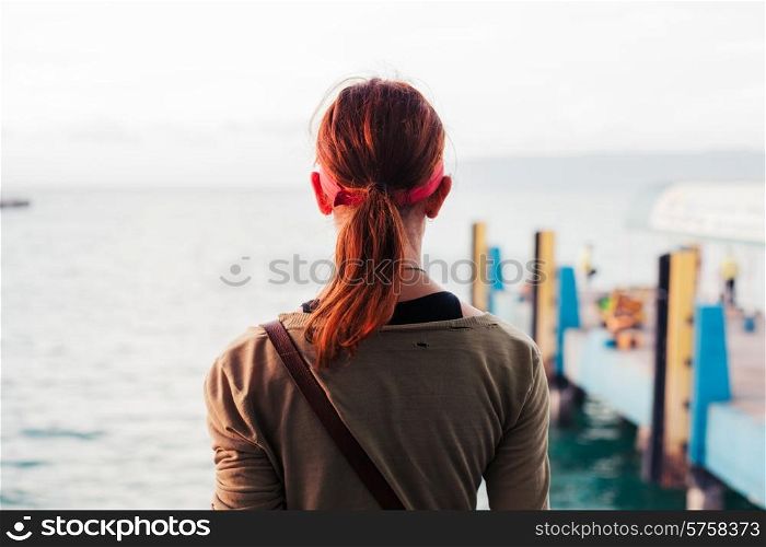 Rear view of a young woman standing by a pier at sunset