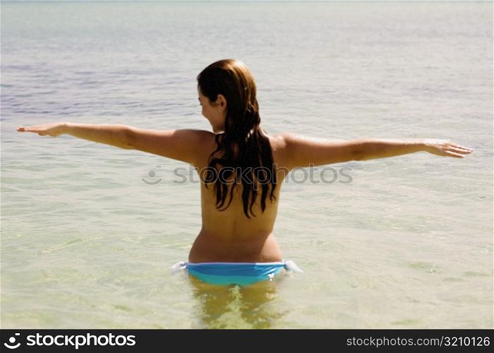 Rear view of a young woman standing with her arm outstretched in water