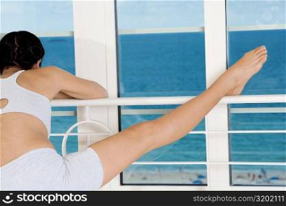 Rear view of a young woman stretching on the railing of a window